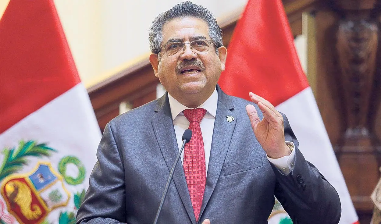 Manuel Merino de Lama habla ante un micrófono entre banderas del Perú.
